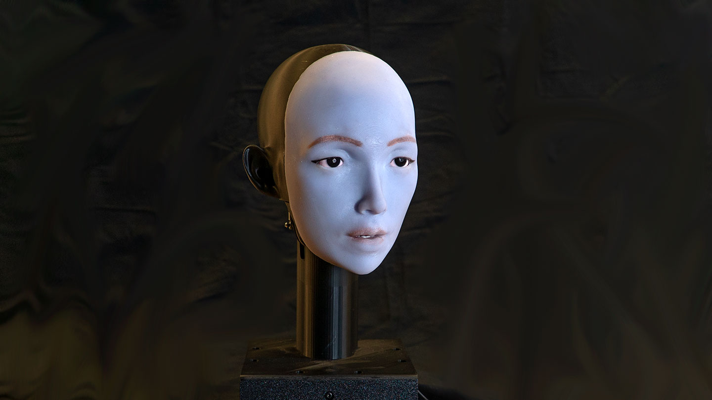 a photo of a humanoid robot face on a rod against a black backdrop