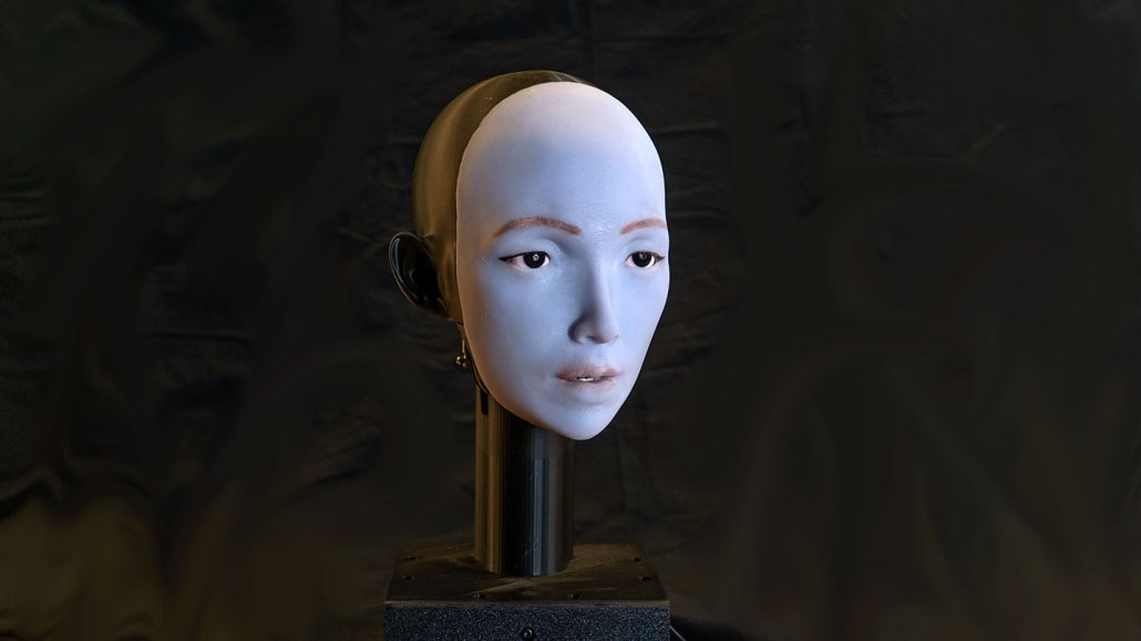 a photo of a humanoid robot face on a rod against a black backdrop