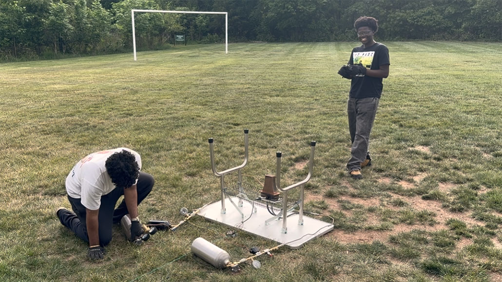 two young men are getting their engine nozzle aparatus ready for a test, they're in a field