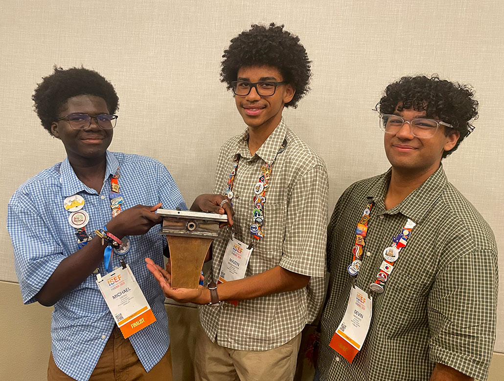 three smiling young black men hold their new aerospike nozzle at ISEF