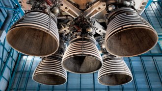 the bottom of the Saturn 5 rocket shows 5 bell shaped rocket engines from the underneath