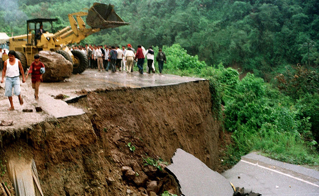 a photo of a people standing in the rain in front of a completely washed out section of road in Bolivia