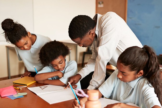 a teacher leans over to explain something to a group of students working at a table