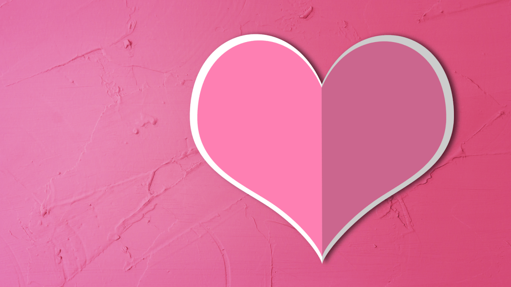 a pink paper cut out heart with a fold line down the middle, against a pink background