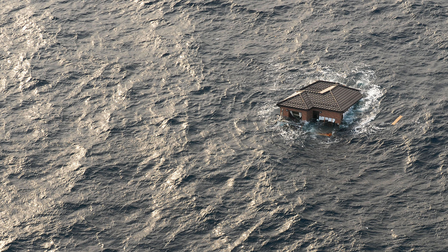 a lone house swept out to sea as seen from the air