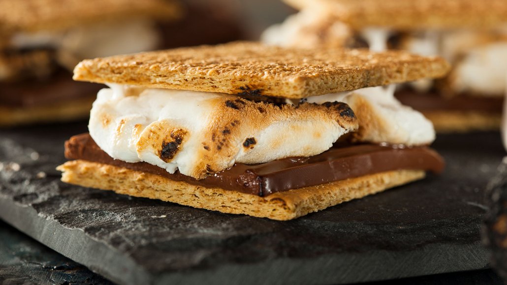 a s'more with a toasted marshmallow sandwiched between graham crackers and chocolate resting on a black surface