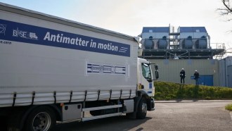 a large white and blue shipping truck with the words "antimatter in motion" on the side pulls up to a building