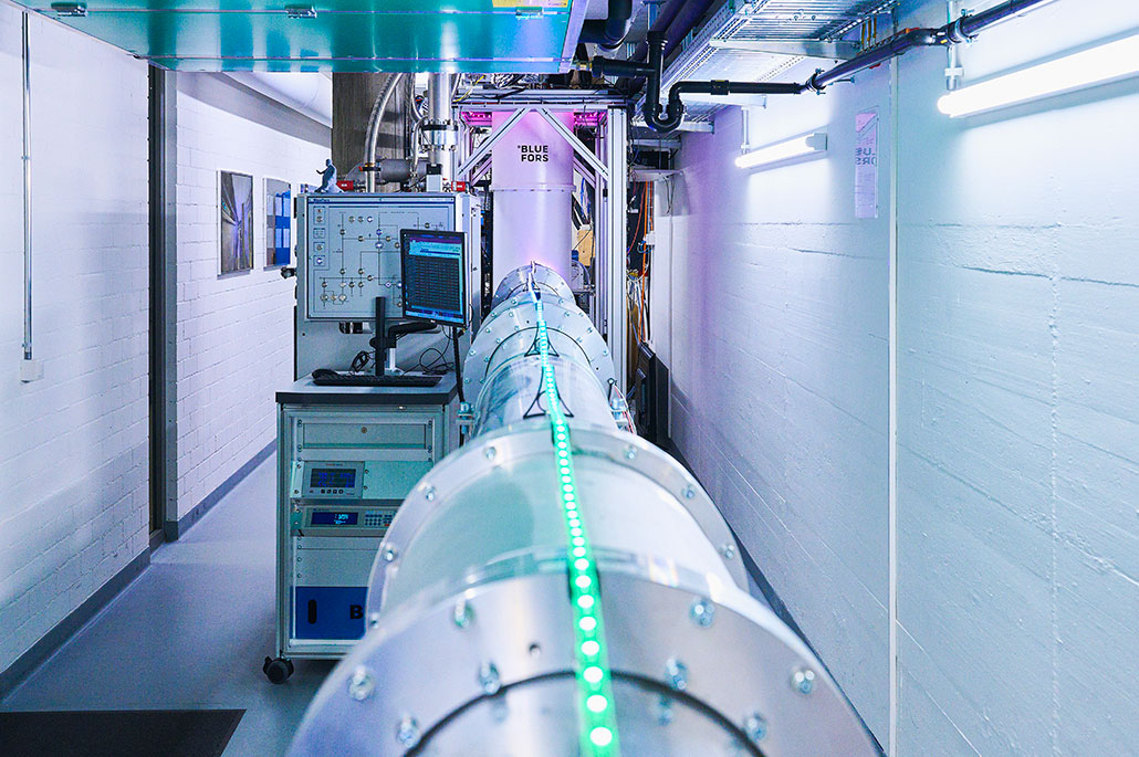 A long silver metal pipe and a stack of electronic equipment take up half of a long hallway