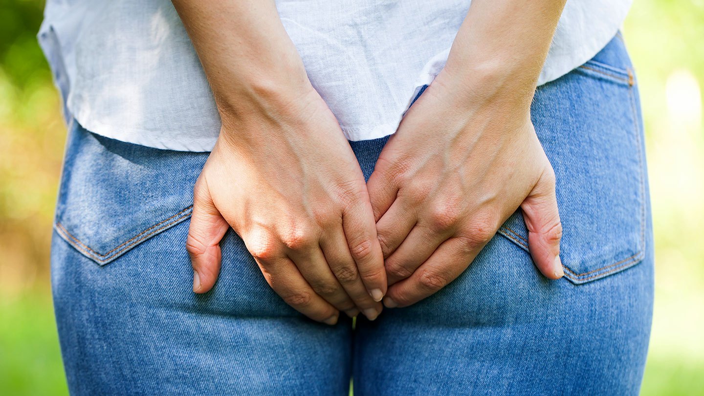 a photo of a person wearing jeans and a white shirt from behind. They are covering their butt as if to stop a fart from coming out.