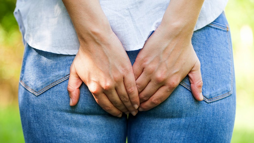 a photo of a person wearing jeans and a white shirt from behind. They are covering their butt as if to stop a fart from coming out.