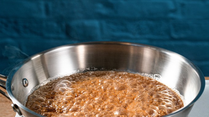 Close up bubbling brown sugar caramelizing in stainless steel pan