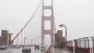 Vehicles and pedestrians cross the Golden Gate Bridge on a foggy damp-looking day.