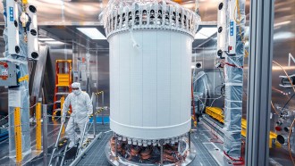 A person stands next to a large cylindrical piece of the LZ dark matter detector