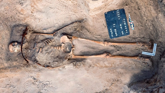 human remains in a shallow excavated grave have a sickle blade placed over the neck and a lock on one foot