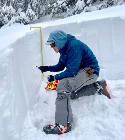 Chris DIckson kneels in a dug out patch of snow. He is measuring the snow layer.