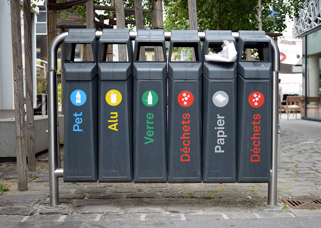 a set of trashbins on a city block, each is designated for a different type of waste