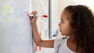 a girl with dark curly hair writes an equation on a whiteboard
