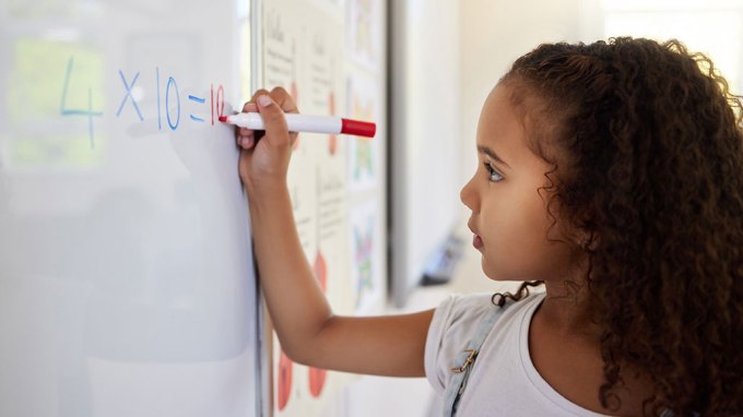 a girl with dark curly hair writes an equation on a whiteboard