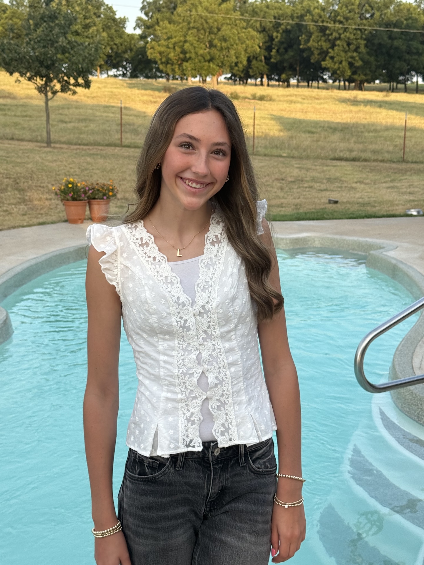 a teen girl smiles standing in front of a pool on a sunny day